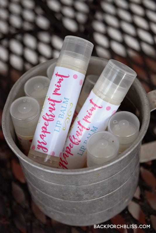 Lip balm tubes with pink grapefruit mint labels standing in a small galvanized bucket on a metal mesh table