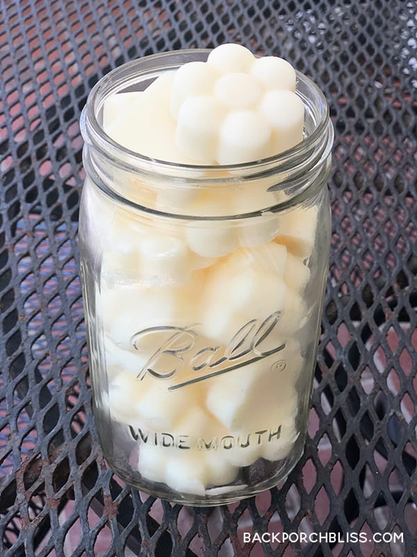A wide mouth mason jar stacked full of pale yellow flower shaped homemade lotion bars on a black metal patio table