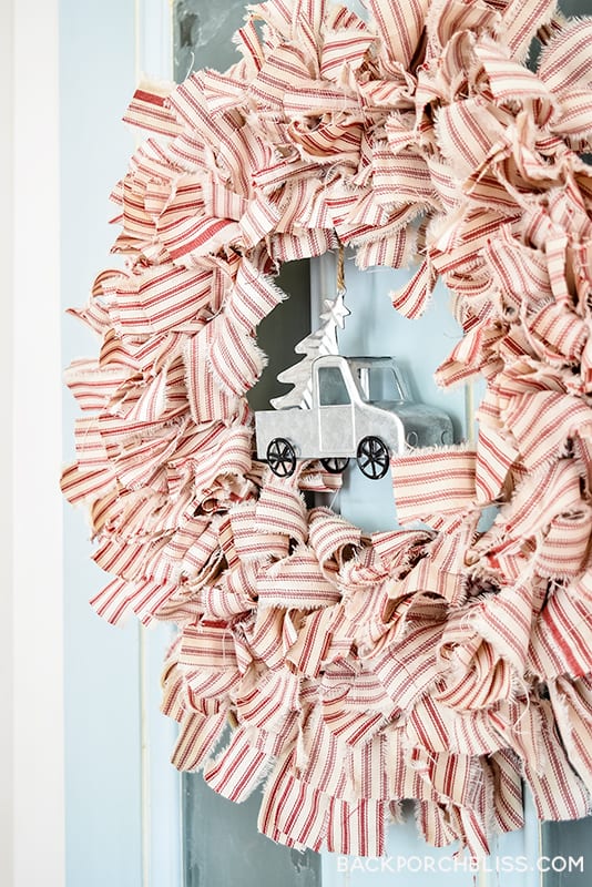A fluffy wreath of red and cream ticking fabric strips with a small galvanized metal truck carrying a tree hung in the center